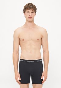 Zwarte katoenen boxershorts met een elastische tailleband met het logo van "Calvin Klein". Gladde textuur en aansluitend design, gedragen door een model.