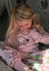 Pink long-sleeve shirt with a playful cat illustration; pink pajama pants featuring colorful cartoon animal patterns. Soft fabric texture.