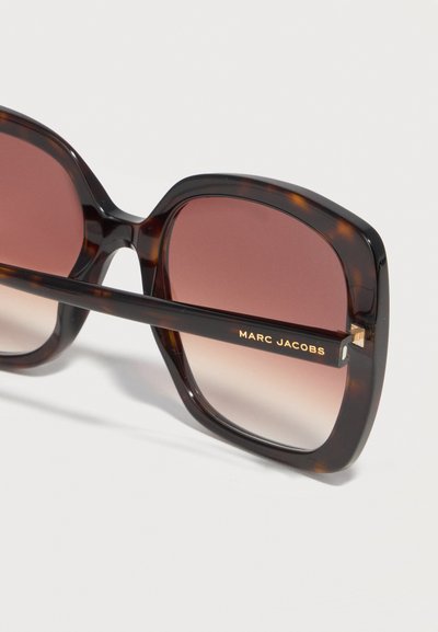 Τετράγωνα γυαλιά ηλίου με σχέδιο χελώνας, φακούς με καφέ διαβάθμιση και το λογότυπο "MARC JACOBS" τυπωμένο σε χρυσό στη βάση.
