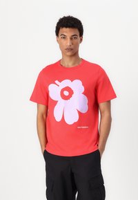 Červené bavlněné tričko s velkým růžovým květinovým motivem a názvem značky "marimekko" vytištěným na spodní části. Kulatý výstřih a krátké rukávy.