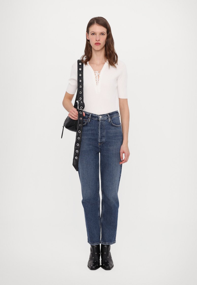 Haut blanc côtelé avec détail à lacets, jeans droit bleu, bottines noires avec accents argentés et sac noir avec anse cloutée.