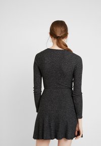 Grå stickad klänning med långa ärmar, åtsittande i midjan och utsvängd kjol. Mjuk, strukturerad tyg med ett subtilt mönster.