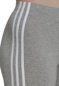 Grijze sportbroek met drie verticale witte strepen aan de zijkant, gemaakt van zachte stof. De tailleband is elastisch voor comfort.