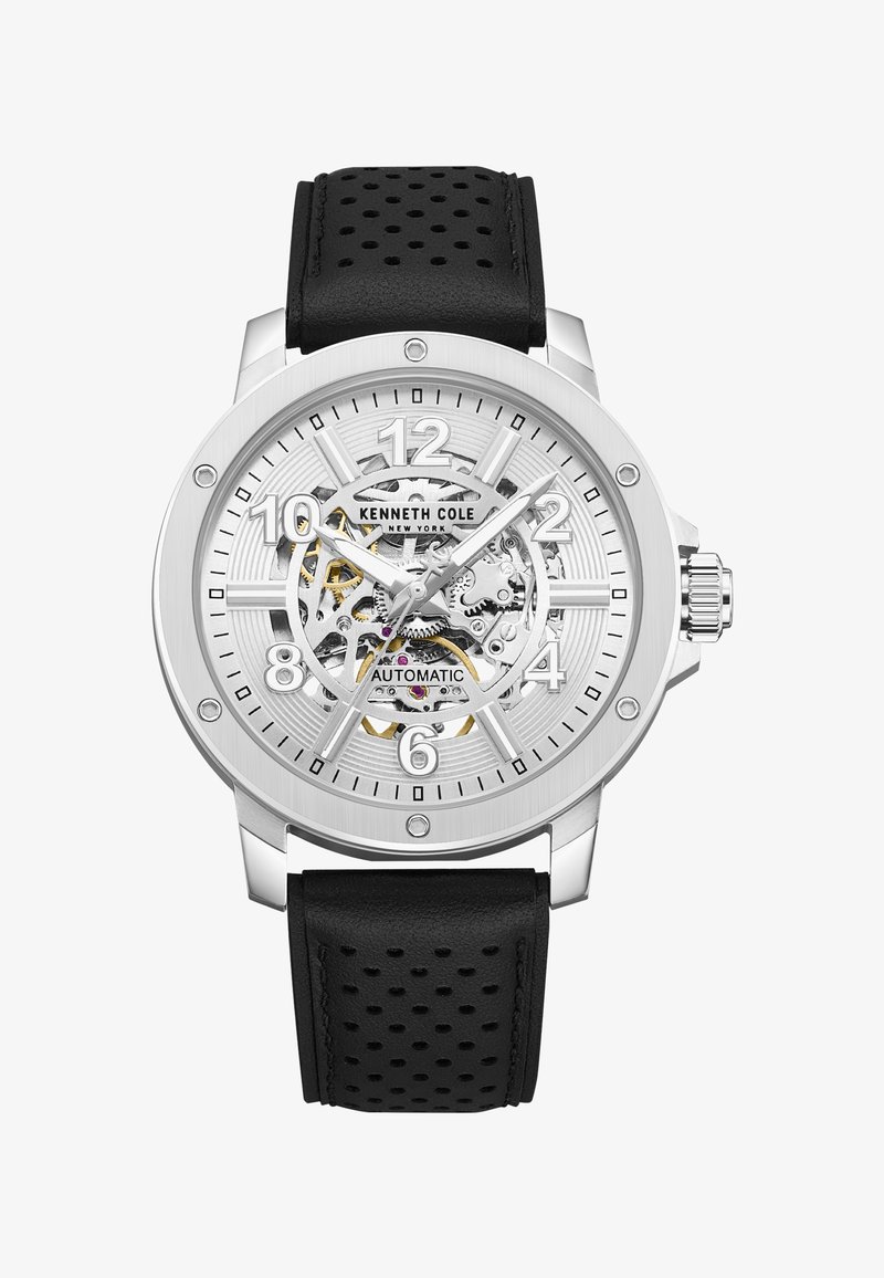 Montre automatique en argent Kenneth Cole avec bracelet en cuir noir perforé et engrenages mécaniques visibles sur le cadran indiquant l'heure 10:10:35.