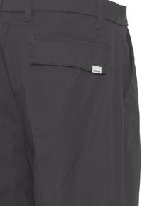 Donkergrijze broek met een gladde textuur, voorzien van een achterzak met een klep en een klein wit label met de tekst "SOLID."