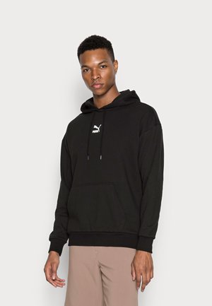 Felpa nera con tasca a marsupio, cappuccio con cordino e logo Puma bianco sul petto. Tessuto morbido, vestibilità rilassata, cuciture in evidenza.