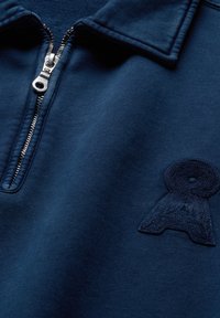 Donkerblauwe sweatshirt met kwartrits, metalen ritssluiting en een geborduurd logo op de borst nabij de kraag.
