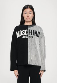 Megztinis su juodais ir pilkais dryžiais, ant kurio bold ryškiomis baltomis raidėmis parašyta "Moschino Jeans". Susikaupus tekstūra, ilgomis rankovėmis, apvaliu kaklu.