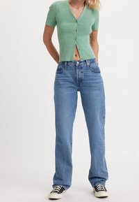 Cárdigan verde menta de manga corta con botones, combinado con jeans de tela vaquera azul de pierna recta y zapatillas negras con suelas blancas.