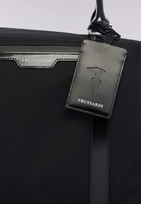 Černá nylonová taška s koženými detaily, elegantním designem a visačkou na zavazadla s vyraženým logem Trussardi.