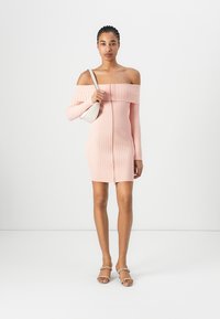 Rosa ribbet av slep-erkje kjole med en tett silhuett, lange ermer og glidelås foran. Modell som holder en liten hvit veske.