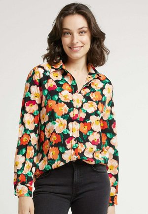 Chemisier floral coloré avec de grandes fleurs orange, rose et blanches sur fond noir. Conception avec boutons, manches longues et col.