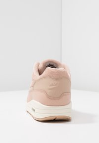 Teniska Nike Air s jemným růžovým svrškem z broušené kůže, koženými detaily a bílou střední podrážkou. Má strukturovaný zadní díl a vyražené logo na patě.