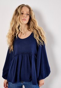 Navyblaues, strukturiertes Oberteil mit Rundhalsausschnitt, langen Ärmeln und gerafftem Taillendetail, kombiniert mit lässigen Jeans.