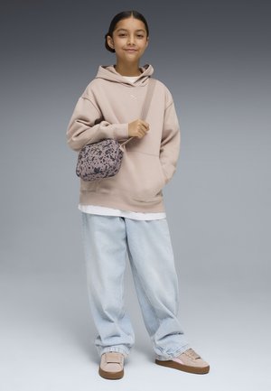 Jeune fille portant un sweat à capuche beige, un jean bleu clair ample, des baskets beige, et portant un sac bandoulière rose à pois noirs.