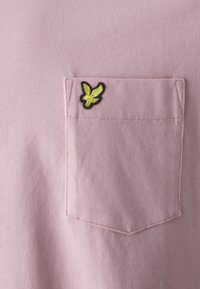 Lys rosa T-skjorte med teksturert overflate, med en lommepatch og en svart omrissgul fuglelogo på lommen.