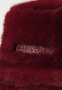 Burgunder falsk pelsprodukt med en glat tekstur, der har et lædermærke prægede med "Hôtel Mahfouf." Blød og fluffy finish.