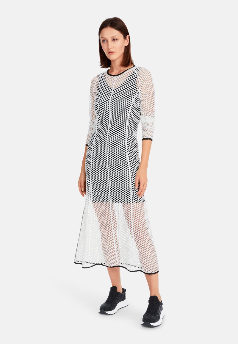 Schwarz-weißes Netzkleid mit dreiviertel Ärmeln, das ein strukturiertes Design, durchsichtigen Stoff und einen knielangen Saum aufweist.