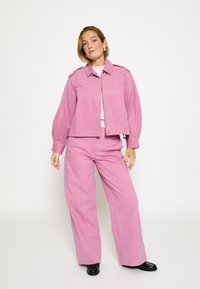 Roza traper jakna s ovratnikom i prednjim džepovima, uparena s širokim ružičastim hlačama. Glatka tekstura, minimalistički dizajn i usklađena shema boja.