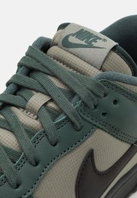 Nike sneakers s zeleno-šedou barevnou kombinací. Vyrobené z kůže a textilu, s texturovaným povrchem a výrazným logem na jazyku.
