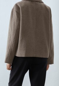 Brun uldblandingsjakke med lige snit, bred krave og tekstureret stof. Har sænkede skuldre og et rent, minimalistisk design.