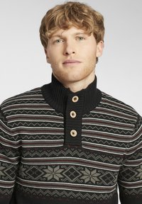 Suéter negro de punto con cuello acanalado, que presenta una tapeta con botones y patrones intrincados de copos de nieve y rayas en gris, blanco y burdeos.