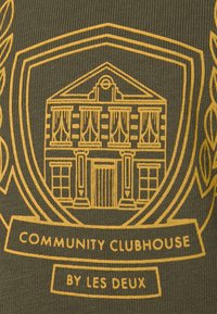 Zelená látka má žlutou grafiku budovy s závěsy, obklopenou designem štítu, a text "COMMUNITY CLUBHOUSE by LES DEUX."