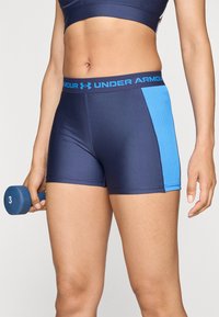 Tumesinine sportlikud lühikesed püksid helesinise aktsentpaneeliga, venivast materjalist, detailse õmblusega ja elastse vöökohaga, millel on silt "Under Armour".
