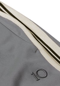 Tissu gris à texture lisse, avec une doublure crème contrastante et des accents rayés noirs. Numéro « 10 » brodé en noir.