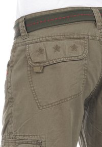 Khaki Cargo-Hosen mit einer bestickten Tasche mit drei Sternen, einem grünen Gürtel mit rotem Nähen und einem strukturierten Stoff.