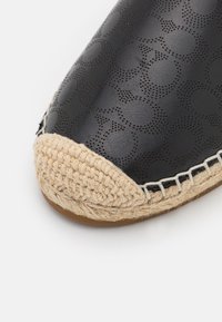 Μαύρο δερμάτινο παπούτσι με περφοραρισμένο σχέδιο, στρογγυλό σχήμα και φυσικό τζούτ toe cap. Ορατές ραφές και υφή επιφάνειας.