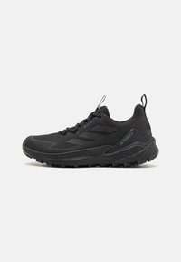 Schwarze Sportschuhe mit einem strukturierten Mesh-Obermaterial, das über einen gepolsterten Schaft, einen Zugreifen und eine robuste Gummisohle für guten Halt verfügt.