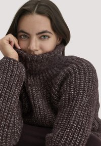 Grob gestrickter Pullover in Dunkellila mit hohem Rollkragen, der über strukturierte Muster verfügt. Weiches Material mit sichtbaren Nahtdetails.