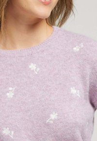 Pull violet clair en matière douce, avec des broderies florales blanches dispersées sur le devant, et un col côtelé.