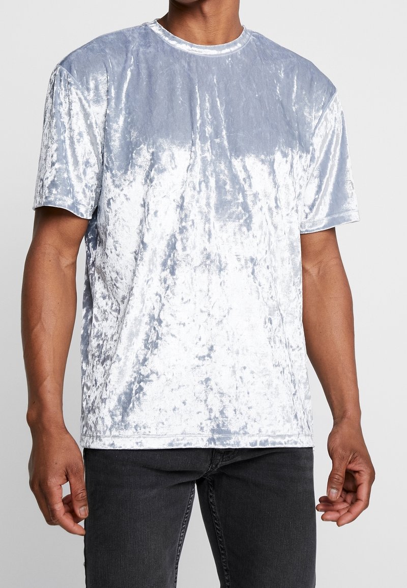 T-shirt bleu clair en velours à manches courtes, avec une texture douce, un col rond et un léger éclat. Porté avec un jean foncé.