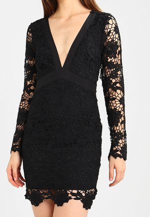 Robe en dentelle noire avec un décolleté en V profond, manches longues ajustées en dentelle florale transparente, et ourlet festonné sur le torse et les bras d'un mannequin féminin.