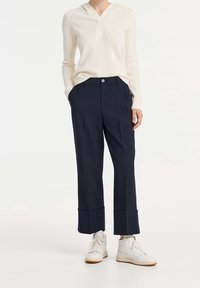 Pullover a coste ribbato color crema con scollo a V; pantaloni tailleur blu navy con orlo risvoltato; sneakers alte bianche.