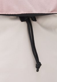 Haut en tissu rose clair avec bordure noire, doté de cordons noirs. Texture lisse avec une légère brillance. Fond blanc uni visible.