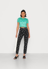 Top curto de renda turquesa com mangas curtas, combinado com jeans pretos de cintura alta com bolinhas brancas, e sand�álias de salto pretas.