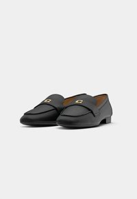 Black leather loafers with a flat heel, featuring a decorative golden hardware accent. Smooth texture and classic slip-on design.