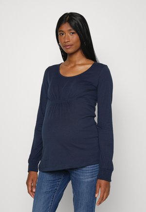 Top de maternidade de manga longa azul-marinho com decote redondo, franzido sob o busto e punhos texturizados. Combinado com jeans de denim azul.
