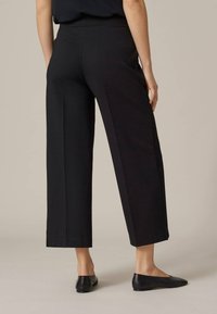 Svarta vida byxor med en slät yta, utrustade med resårmidja och knäholkar. Bärs med svarta ballerina-skor.