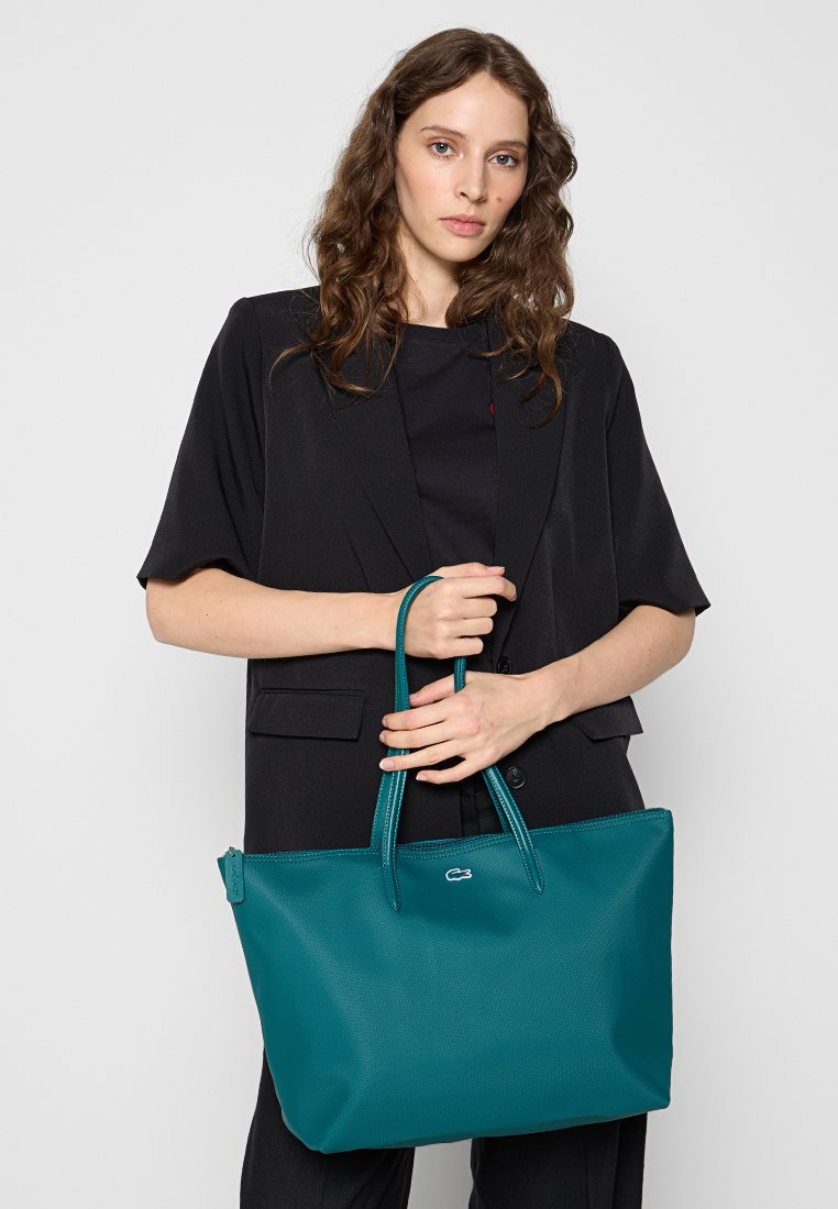 Bolso tote de cuero en color teal con superficie texturizada, asas dobles y un detalle de logo. El bolso es espacioso y tiene una forma rectangular.