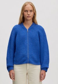 Blauwe gebreide cardigan met ritssluiting aan de voorkant, geribbelde textuur en oversized mouwen. Heeft een ronde halslijn en subtiele gemêleerde details.