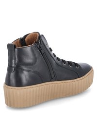 Svart hög sneakers med tan-randig plattformssula, sidogång, snörning framtill och mjukt innerfoder synligt vid anklekragen.