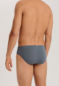 Grijze katoenen slips met een gladde textuur, elastische tailleband en een aangesloten ontwerp, weergegeven vanuit een achterperspectief.