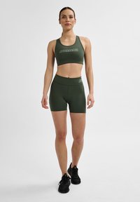 Olivgrüner Sport-Bra mit Logo und passenden, hochtaillierten Shorts. Glattes, dehnbare Material, das für Komfort und Bewegungsfreiheit sorgt.