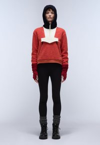 Rød og sort fleece hoodie med beige panel, lynlås og manchetter, parret med sorte leggings og kraftige sorte støvler. Teksturområde.