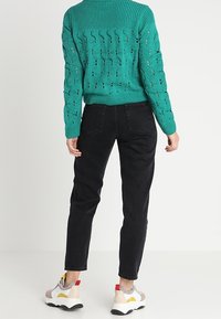 Turkos stickad tröja med ett strukturerat mönster, tillsammans med svarta åtsittande jeans och flerfärgade sneakers med inslag av röd och gul.