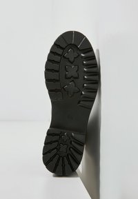 Suola di scarpa in gomma nera con un motivo di battistrada testurizzato e accenti a forma di croce, che offrono trazione e stabilità.